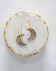 Gold leather crescent moon earrings with gold hooks, displayed on a white marble tray with gold edging