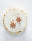 Rose gold leather star earrings with gold hooks, displayed on a round white marble tray with gold edging