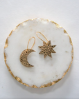 Metallic bronze leather moon and star earrings with gold hooks, styled on a white and gold-edged marble display