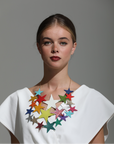 Front view of model wearing large layered multicoloured leather star necklace with gold chain, styled with a white V-neck top
