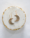 Gold leather crescent moon earrings with gold hooks, displayed on a white marble tray with gold edging