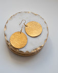 Grian leather earrings in metallic gold – circular statement earrings displayed on a marble and gold dish