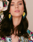 Model wearing layered leather leaf earrings in mustard yellow and navy, styled with a bold patterned dress and dark loose waves