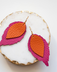 Layered leather earrings in orange and magenta pink, handcrafted from Italian top-grain leather and photographed on a white marble dish with gold trim
