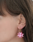 Close-up of a woman wearing a pink and white patterned leather star earring with gold hook, highlighting the bold colours and graphic design against her hair and skin