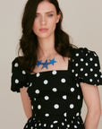 Model wearing the Réalt Star Necklace with three bold blue leather stars, styled with a black and white polka dot dress