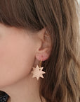 Close-up of a woman wearing a single rose gold leather star earring with gold hook, showing the earring's size and texture against her skin and hair