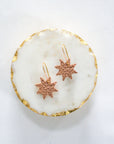 Rose gold leather star earrings with gold hooks, displayed on a round white marble tray with gold edging