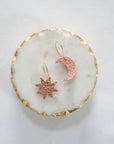 Rose gold leather star and crescent moon earrings with gold hooks, displayed on a white marble tray with gold edging