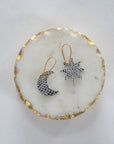 Silver leather moon and star earrings with gold hooks, displayed on a round white marble tray with gold trim