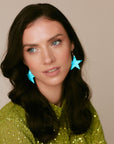 Model wearing bold turquoise leather star earrings with gold-tone hooks, styled with a green sequinned outfit and soft waves