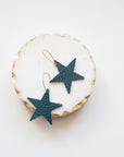 Pair of dark teal leather star earrings with gold hooks displayed on a round white and gold marble-effect dish