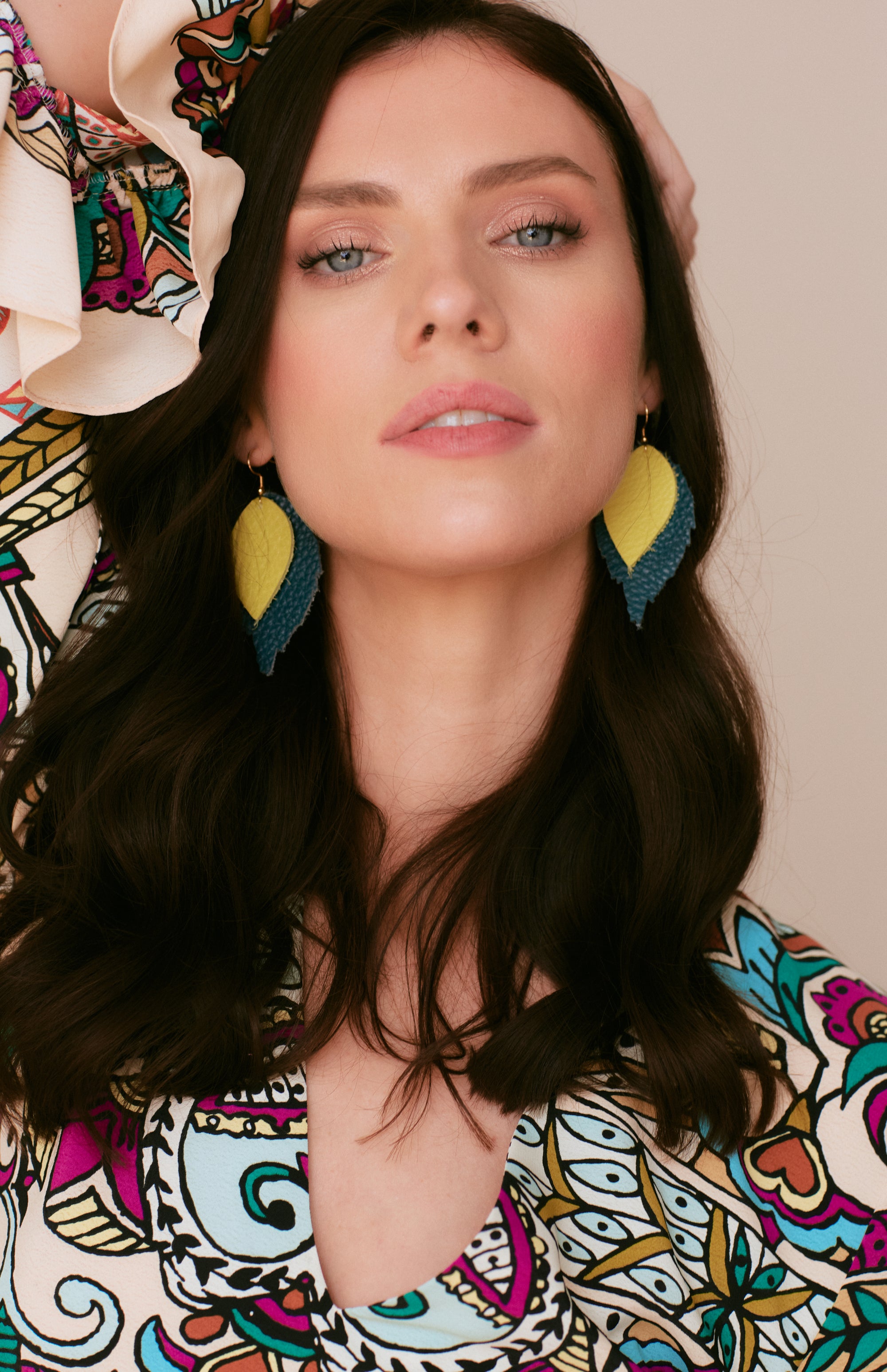Model wearing layered leather leaf earrings in mustard yellow and navy, styled with a bold patterned dress and dark loose waves