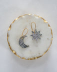 Silver leather moon and star earrings with gold hooks, displayed on a round white marble tray with gold trim