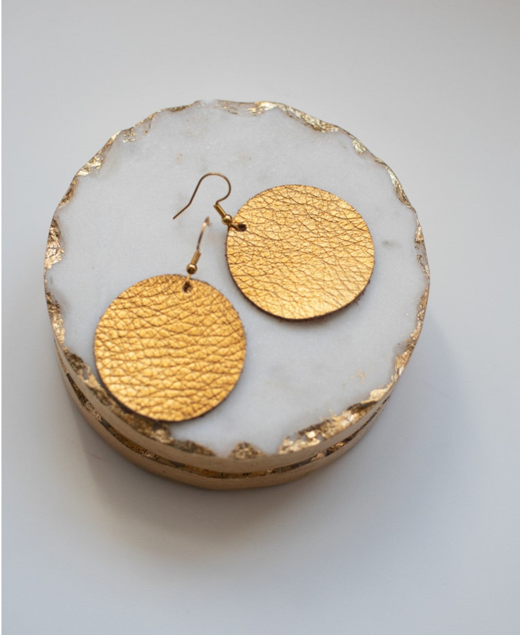 Grian leather earrings in metallic gold – circular statement earrings displayed on a marble and gold dish