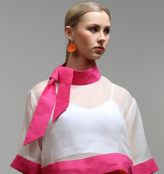 Model wearing bold orange Grian leather earrings with circular shape and gold hooks, styled with a sheer white and hot pink outfit and pink neck tie