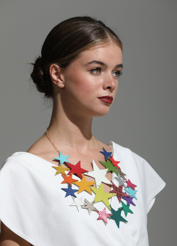Model wearing a statement star necklace in multicoloured Italian leather with layered stars on gold chain, styled with a white top