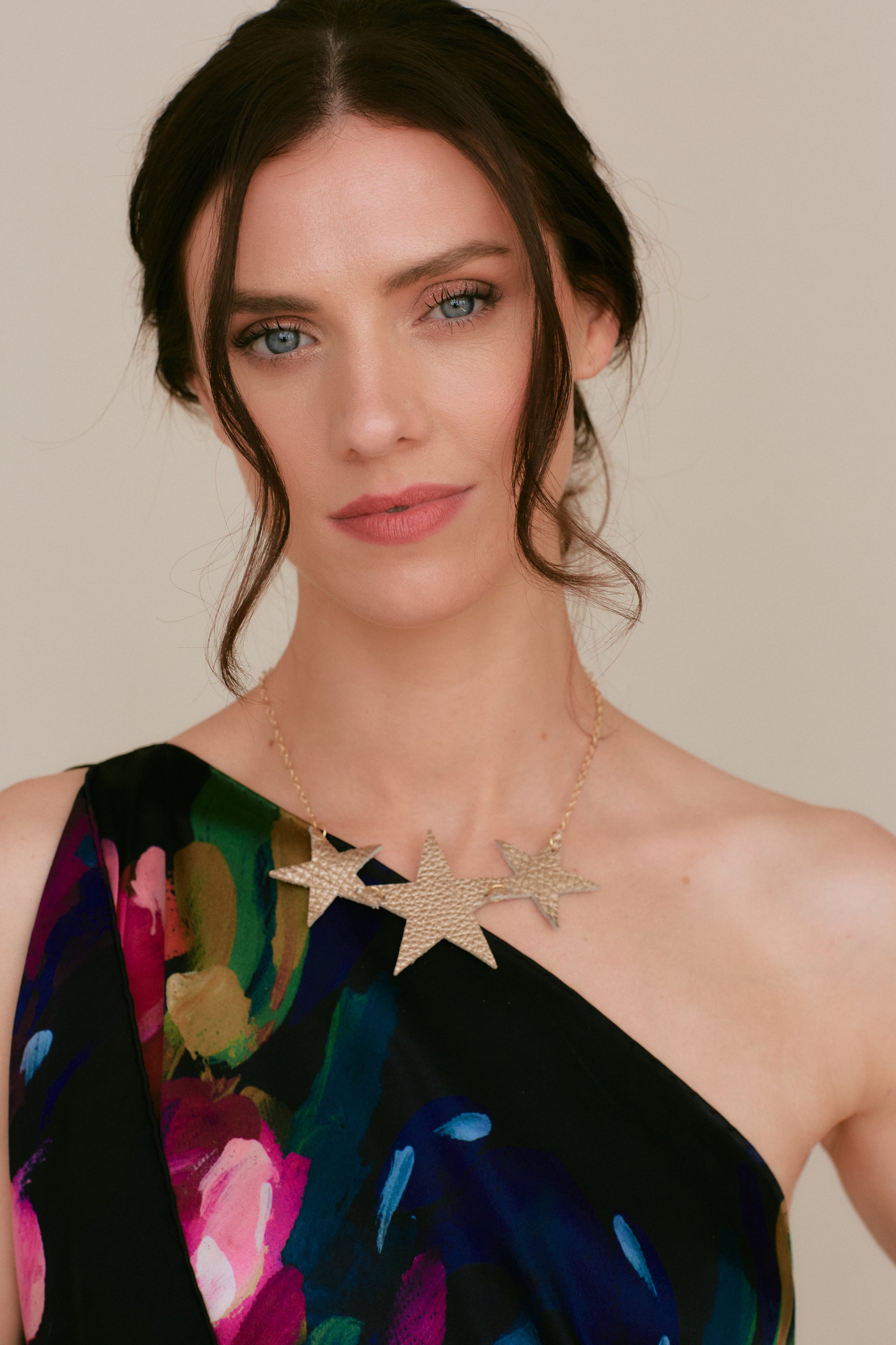 Model wearing the Réalt Star Necklace in gold leather, styled with a one-shoulder floral dress for a statement look