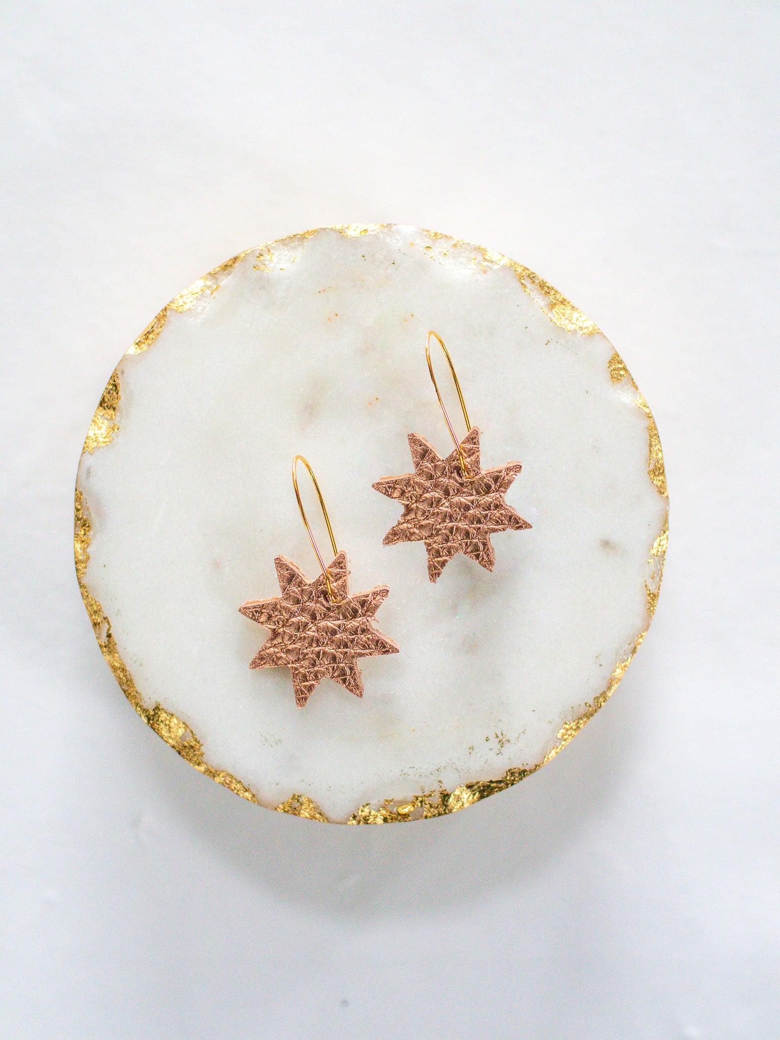 Rose gold leather star earrings with gold hooks, displayed on a round white marble tray with gold edging